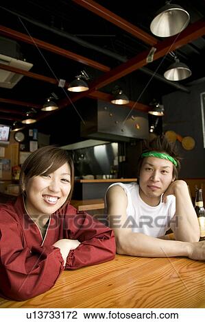 Stock Image - Young man and woman sitting at table. Fotosearch