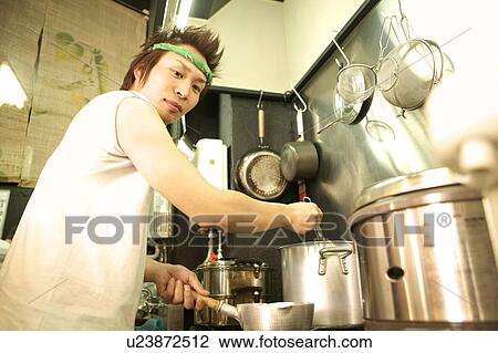 Stock Image - Young man cooking in restaurant kitchen. Fotosearch