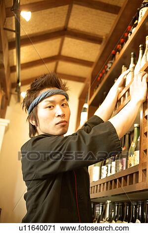 Stock Image - Young man standing in front of shelf. Fotosearch