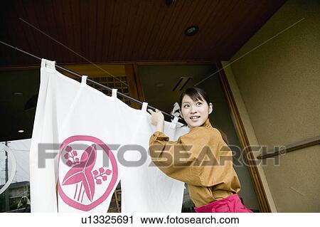 Stock Image - Young woman setting store curtain. Fotosearch