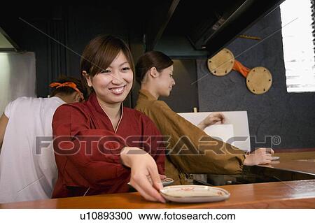Stock Image - Young women working in restaurant kitchen. Fotosearch