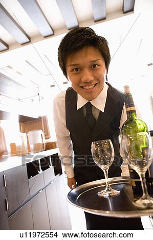 Picture - Waiter carrying bottle of wine and glasses on tray. Fotosearch