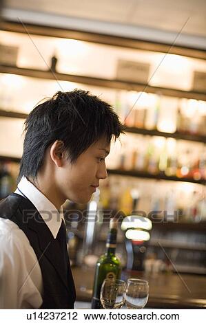 Stock Image - Waiter carrying bottle of wine and glasses on tray. Fotosearch