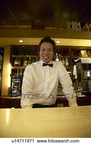 Stock Image - Waiter standing behind bar counter. Fotosearch
