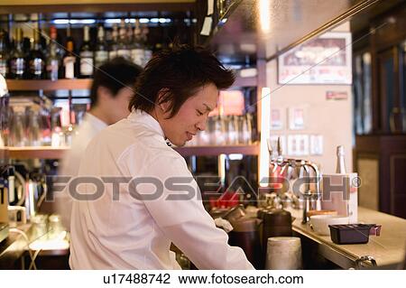 Stock Image - Waiter standing behind bar counter. Fotosearch