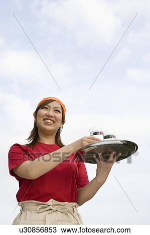 Stock Image - Waitress carrying drinks on tray. Fotosearch