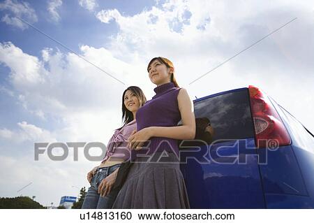 Two young women leaning against car View Large Photo Image Stock Image - Two young women leaning against car. Fotosearch