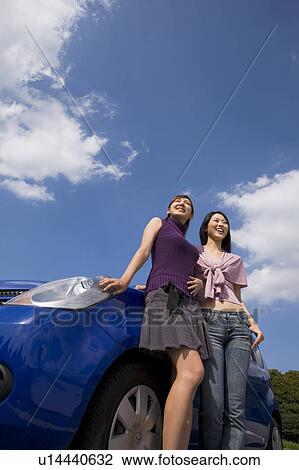 Stock Image - Two young women standing beside car. Fotosearch