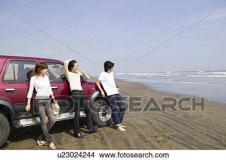 Picture - Young people leaning against car on beach. Fotosearch