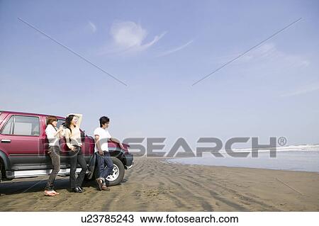 Stock Image - Young people leaning against car on beach. Fotosearch