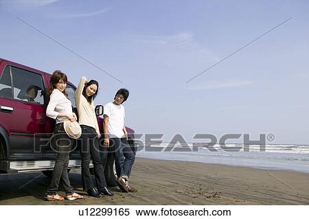 Stock Photography - Young people leaning against car on beach. Fotosearch