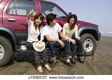 Stock Photo - Young people sitting on side of car. Fotosearch