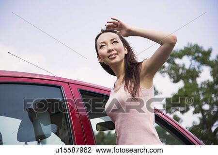 Stock Image - Young woman looking up, shielding eyes. Fotosearch