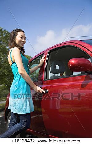 Stock Image - Young woman standing beside car. Fotosearch