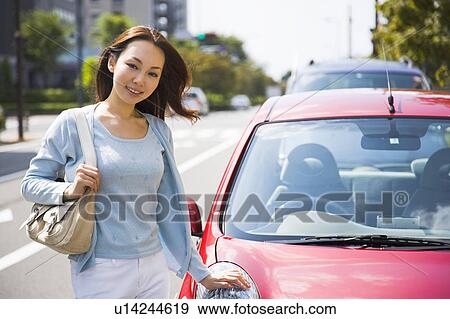 Stock Photo - Young woman standing beside car. Fotosearch