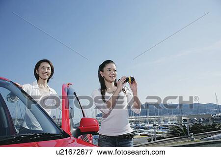 Stock Photo - Two young women getting out of car by marina. Fotosearch