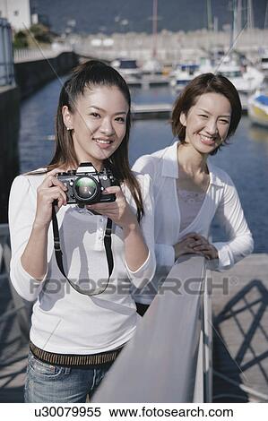 Stock Photography - Two young women in marina, one with camera. Fotosearch