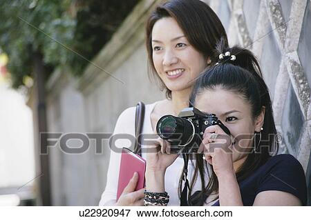 Stock Photo - Two young women, one taking photograph. Fotosearch