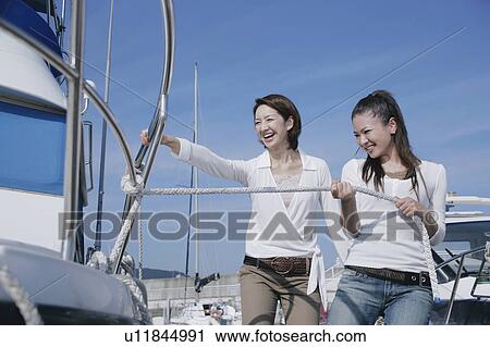 Stock Image - Two young women pulling rope attached to yacht. Fotosearch
