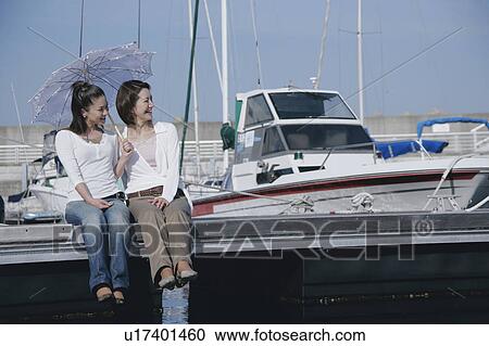 Two young women sitting on pier View Large Photo Image Stock Image - Two young women sitting on pier. Fotosearch