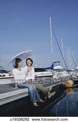 Stock Image - Two young women sitting on pier. Fotosearch