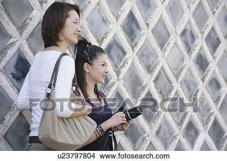 Picture - Two young women standing by wall. Fotosearch