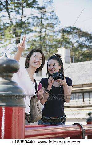 Two young women standing on bridge, one with camera View Large Photo Image Stock Image - Two young women standing on bridge, one with camera. Fotosearch