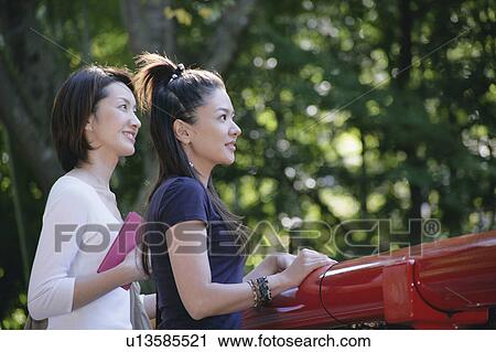 Stock Image - Two young women standing on bridge. Fotosearch