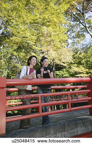 Two young women standing on bridge View Large Photo Image Stock Photography - Two young women standing on bridge. Fotosearch