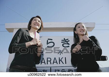 Stock Image - Two young women standing on train platform. Fotosearch
