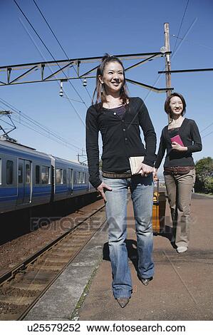 Stock Image - Two young women walking on train platform. Fotosearch