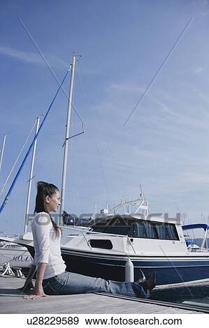 Stock Photo - Young woman sitting on pier. Fotosearch