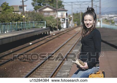Picture - Young woman sitting on suitcase on train platform. Fotosearch