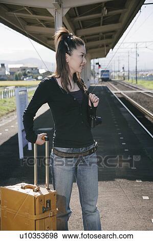 Stock Photo - Young woman standing on train platform with suitcase. Fotosearch