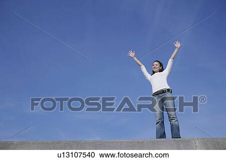 Stock Image - Young woman standing with her arms outstretched. Fotosearch