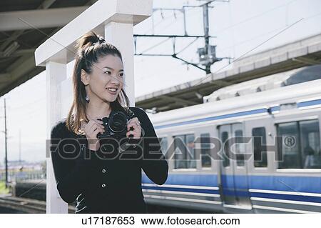 Stock Image - Young woman taking photograph on train platform. Fotosearch
