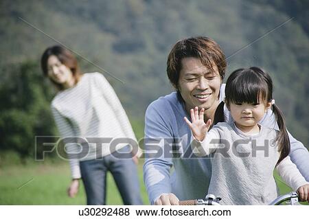 Stock Photo - Father and daughter riding bike in meadow. Fotosearch