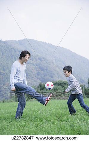Stock Photo - Father and son playing soccer in meadow. Fotosearch