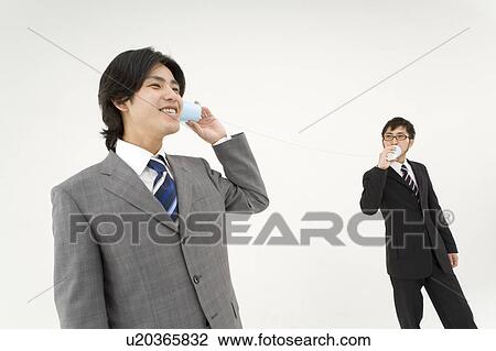 Stock Image - Two young businessmen talking with string and cups. Fotosearch