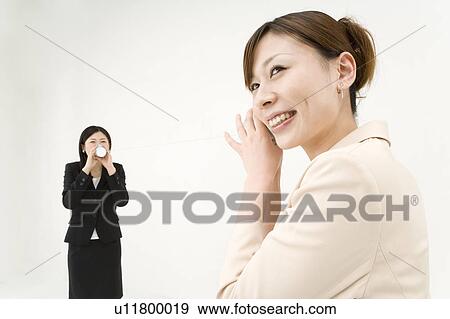Stock Photo - Two young businesswomen talking with string and cups. Fotosearch