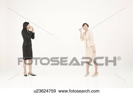 Stock Photo - Two young businesswomen talking with string and cups. Fotosearch