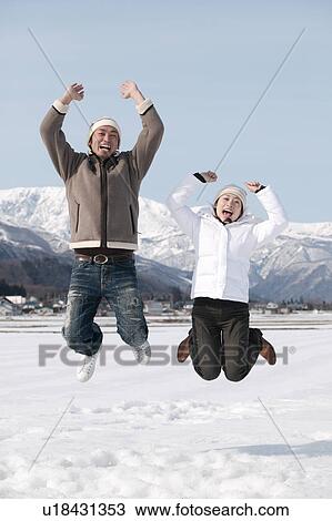 Stock Image - Young couple jumping in snow. Fotosearch