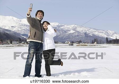 Stock Image - Young couple taking photo with mobile phone. Fotosearch