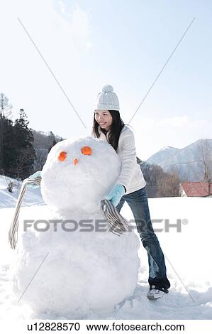Stock Image - Young woman putting scarf on snowman. Fotosearch