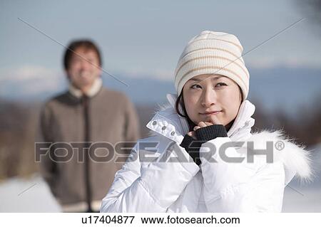 Stock Photo - Young woman smiling, boyfriend in background. Fotosearch