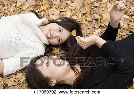 Two young women lying on fallen leaves View Large Photo Image Stock Image - Two young women lying on fallen leaves. Fotosearch