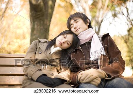 Stock Photograph - Young couple sitting and sleeping on bench. Fotosearch