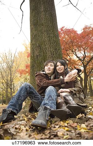 Young couple sitting by tree View Large Photo Image Stock Image - Young couple sitting by tree. Fotosearch