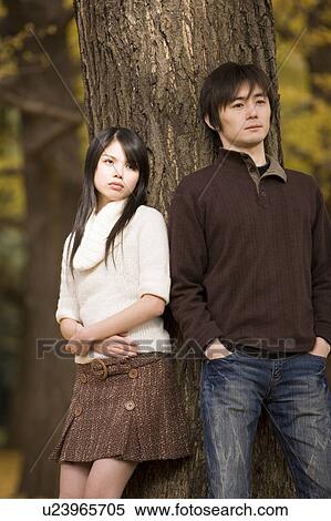 Stock Photography - Young couple standing by tree. Fotosearch