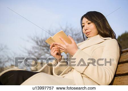 Stock Photo - Young woman reading book on bench. Fotosearch